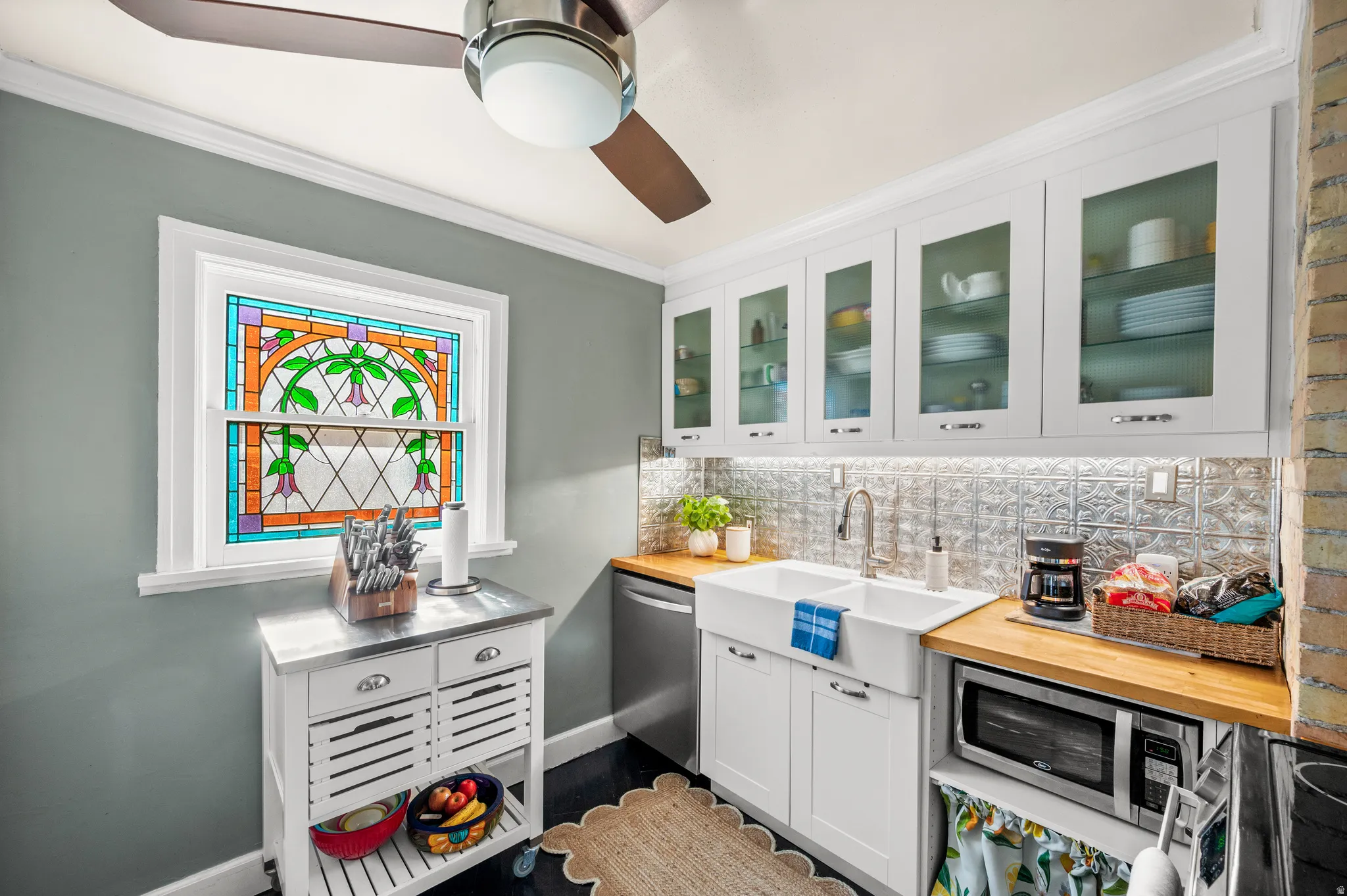 Kitchen featuring a decorative stained glass window, white shaker-style cabinetry with glass inserts, pressed tin backsplash, wood-finish countertops, and a white farmhouse sink
