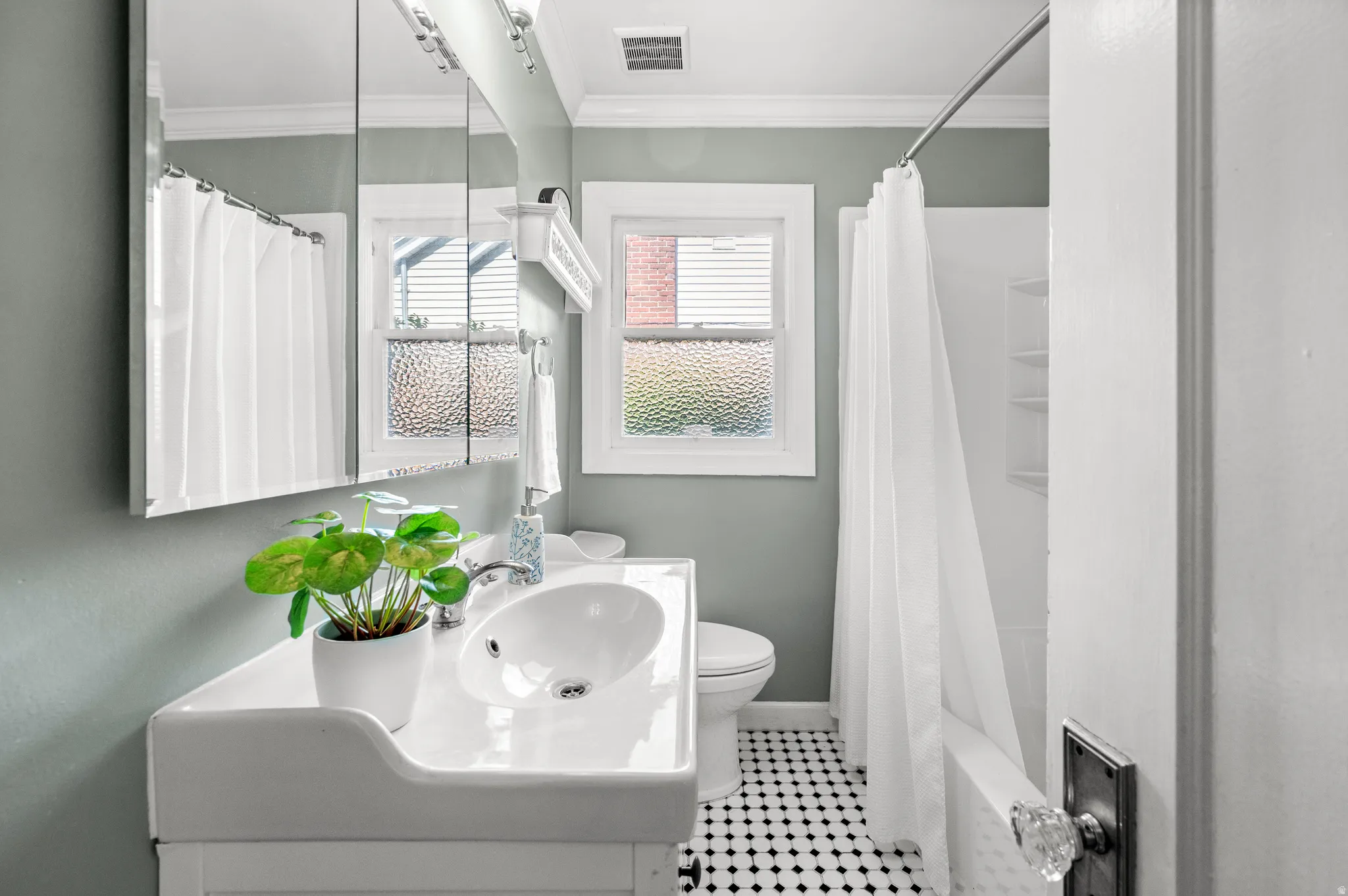Bathroom featuring a white vanity with integrated sink, black and white mosaic tile flooring, a window with textured glass, and a white tub/shower combination