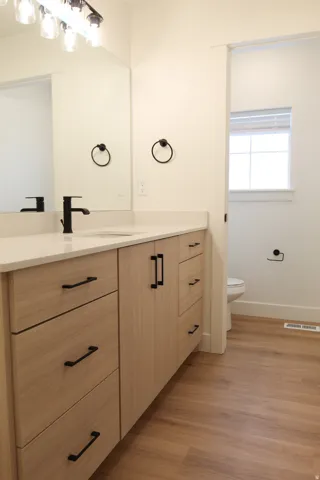 Bathroom vanity featuring light wood-finish cabinetry with black hardware, a light-toned countertop, and an integrated sink with a matte black faucet
