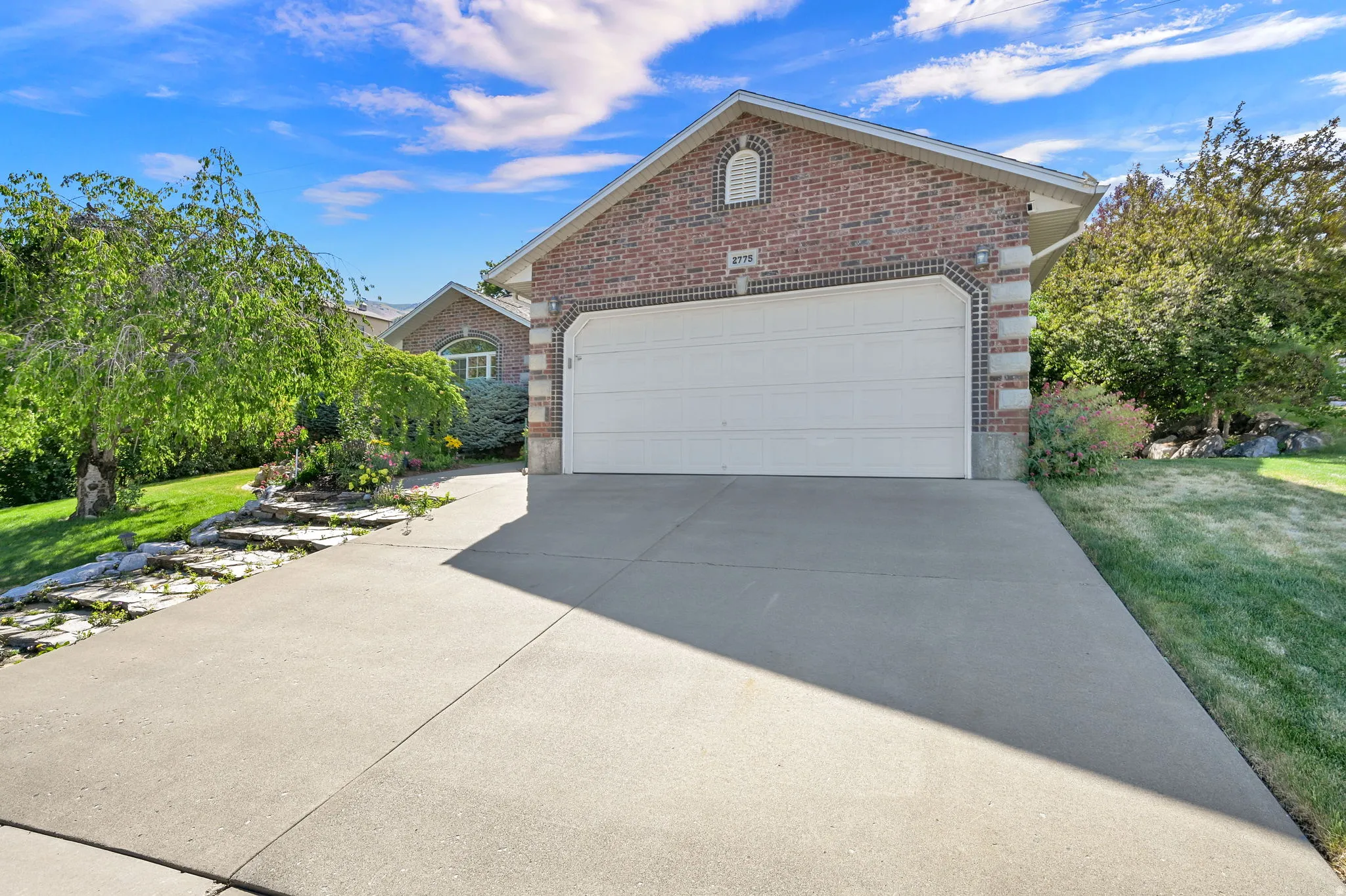 Brick facade residence featuring a two-car garage, concrete driveway, and established landscaping