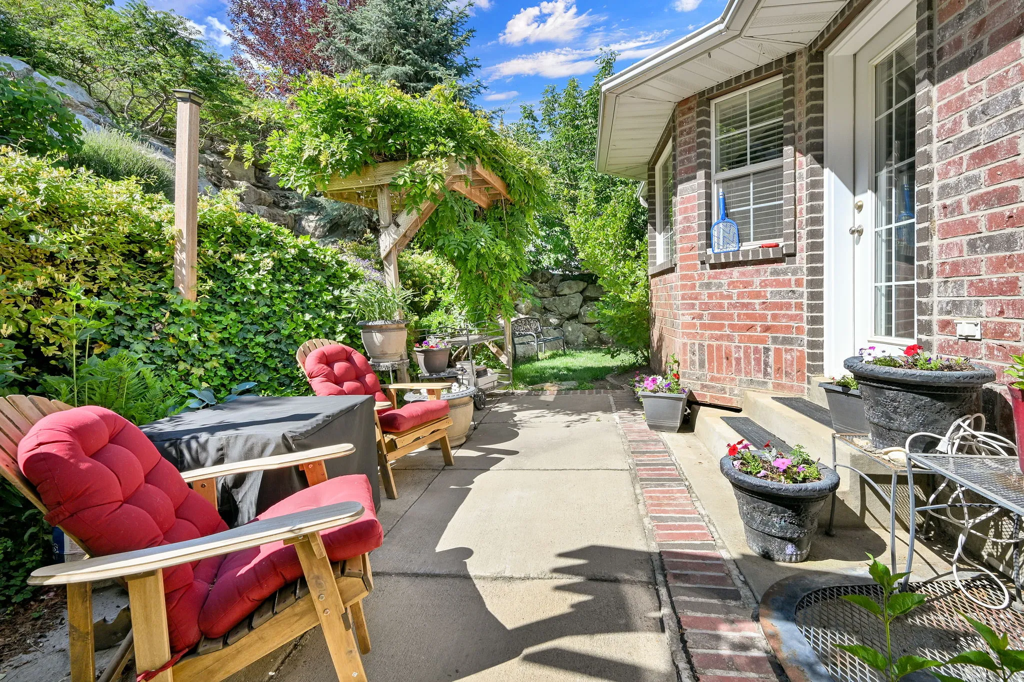 Expansive concrete patio with brick border, featuring a covered pergola structure and a terraced natural landscape