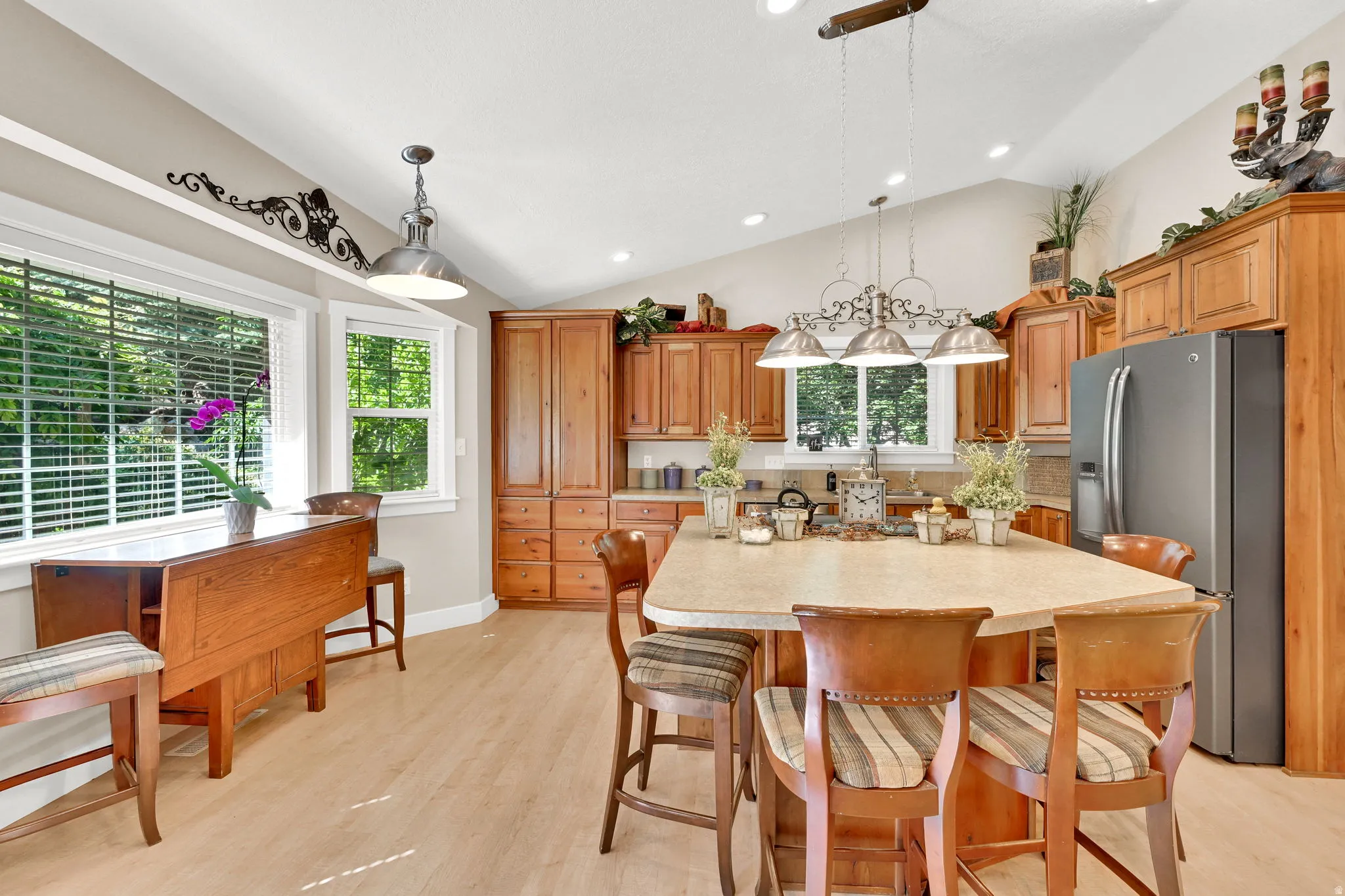 Spacious kitchen featuring warm wood cabinetry, a large center island with seating, stainless steel refrigerator, and light wood-finish flooring