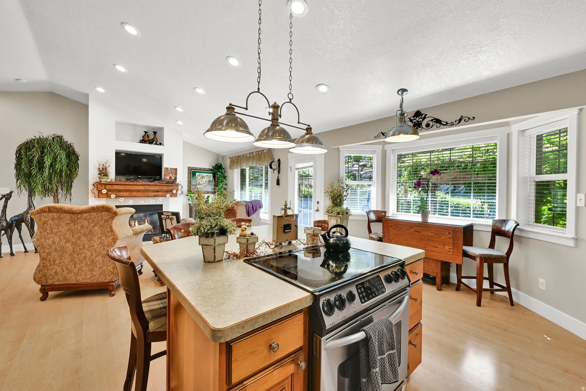 Kitchen island with integrated stainless steel range, light-toned wood-finish flooring, recessed lighting, vaulted ceilings, and a bay window