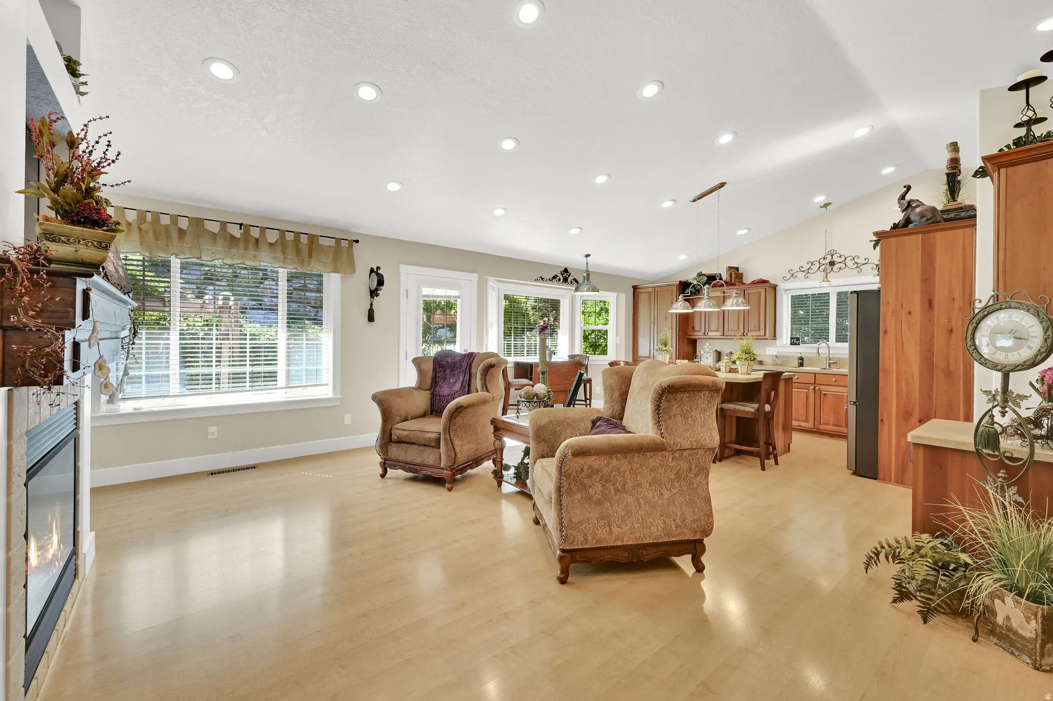 Open-concept interior featuring light wood-finish flooring, recessed lighting, a built-in fireplace, and a kitchen with wood cabinetry and an island