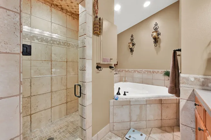Tiled shower enclosure with glass surround, integrated lighting, and a built-in corner soaking tub with tiled surround