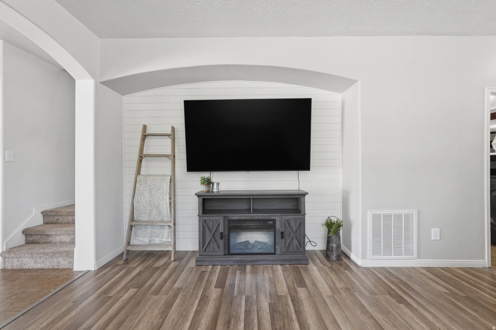 Living area featuring wood-finish flooring and a built-in entertainment niche with shiplap-style accent wall
