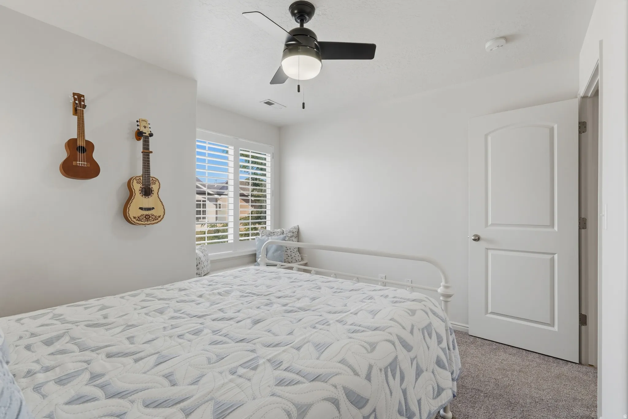 Bedroom featuring a window with plantation shutters, a black ceiling fan with integrated lighting, a white paneled interior door, and gray carpet flooring