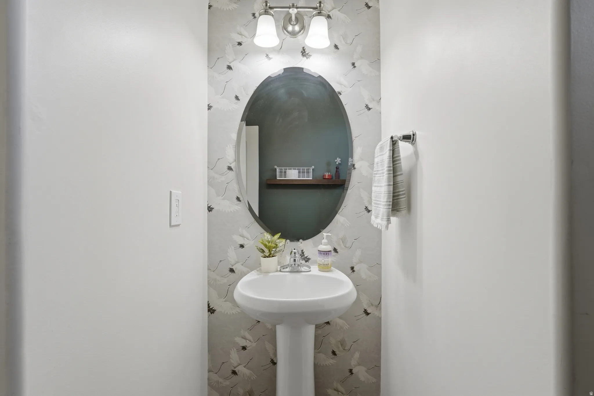 Pedestal sink with a wall-mounted faucet and an oval mirror