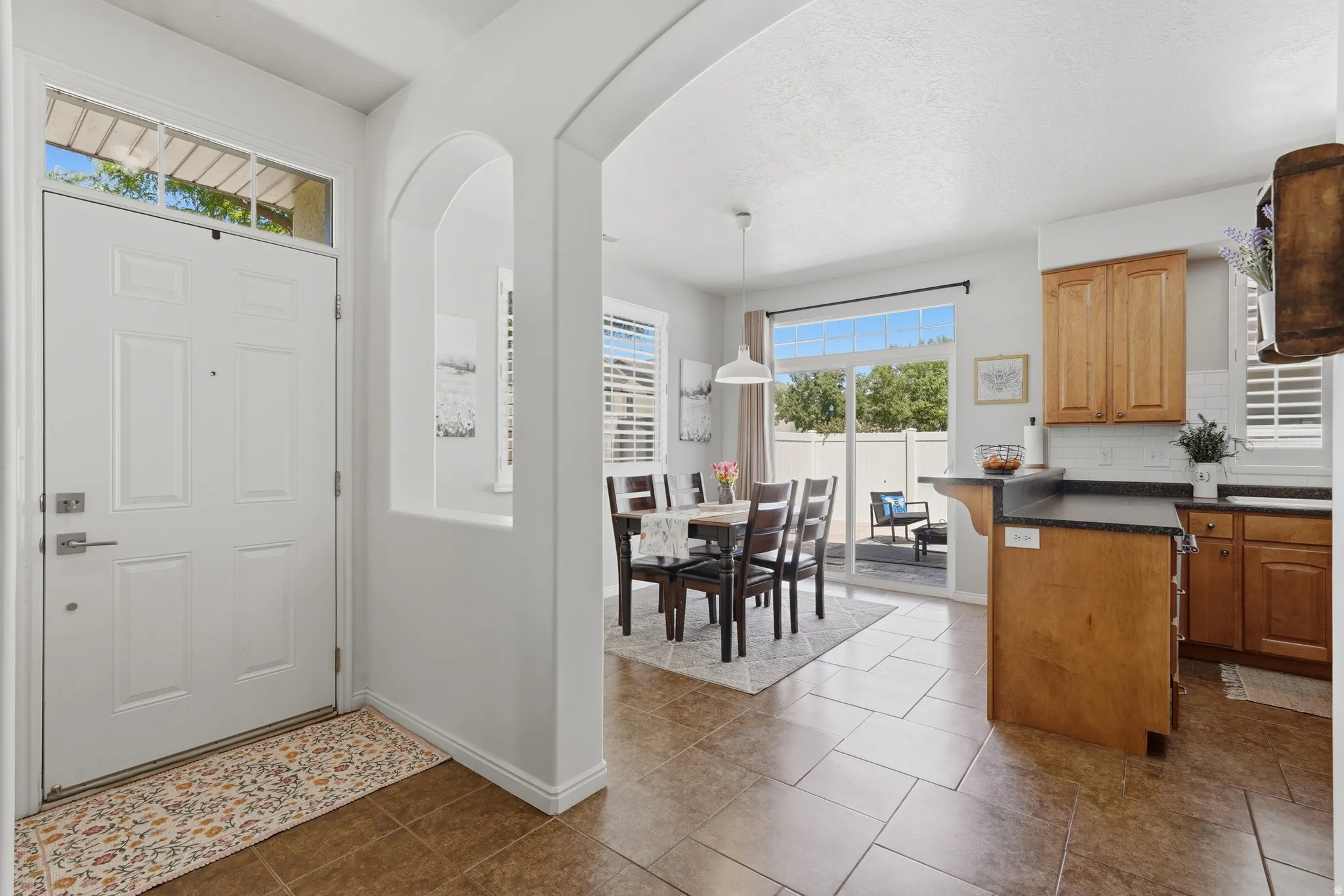 Entryway featuring a transom window, leading to a dining area with sliding glass doors to the patio, kitchen with wood cabinetry, and tile flooring throughout
