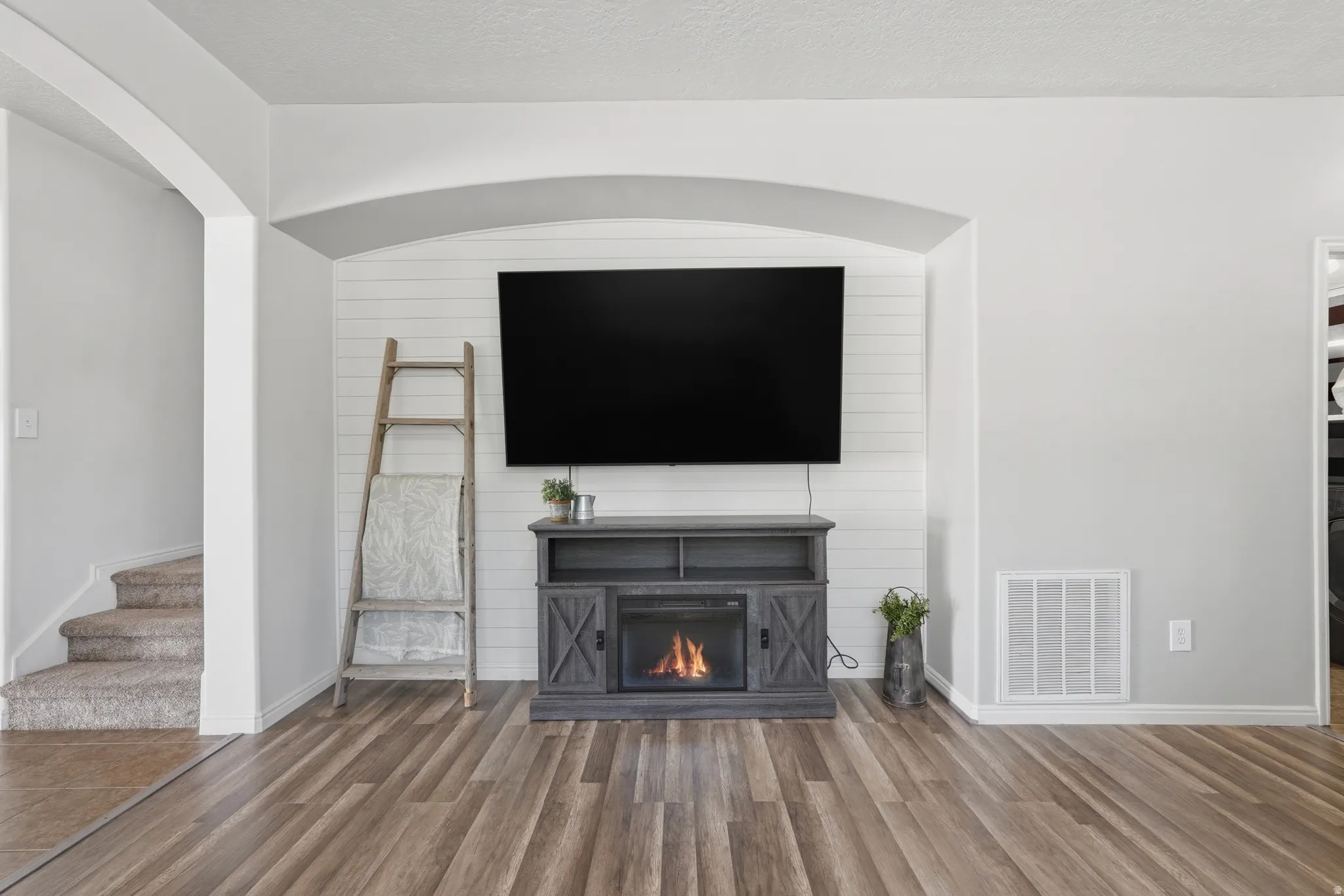 Living area featuring wood-finish flooring, a built-in electric fireplace with shiplap accent wall, and arched doorways