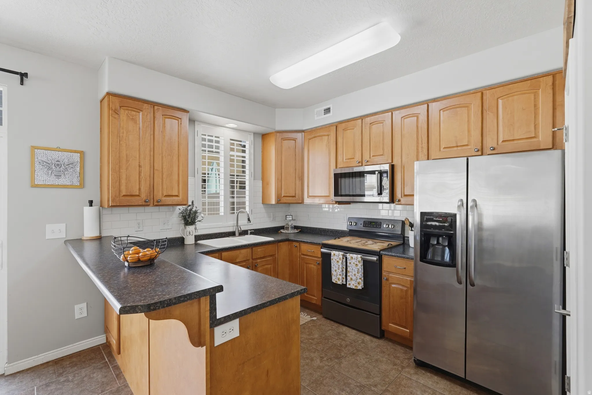Kitchen featuring wood cabinetry, dark countertops, a white subway tile backsplash, stainless steel appliances, and a breakfast bar