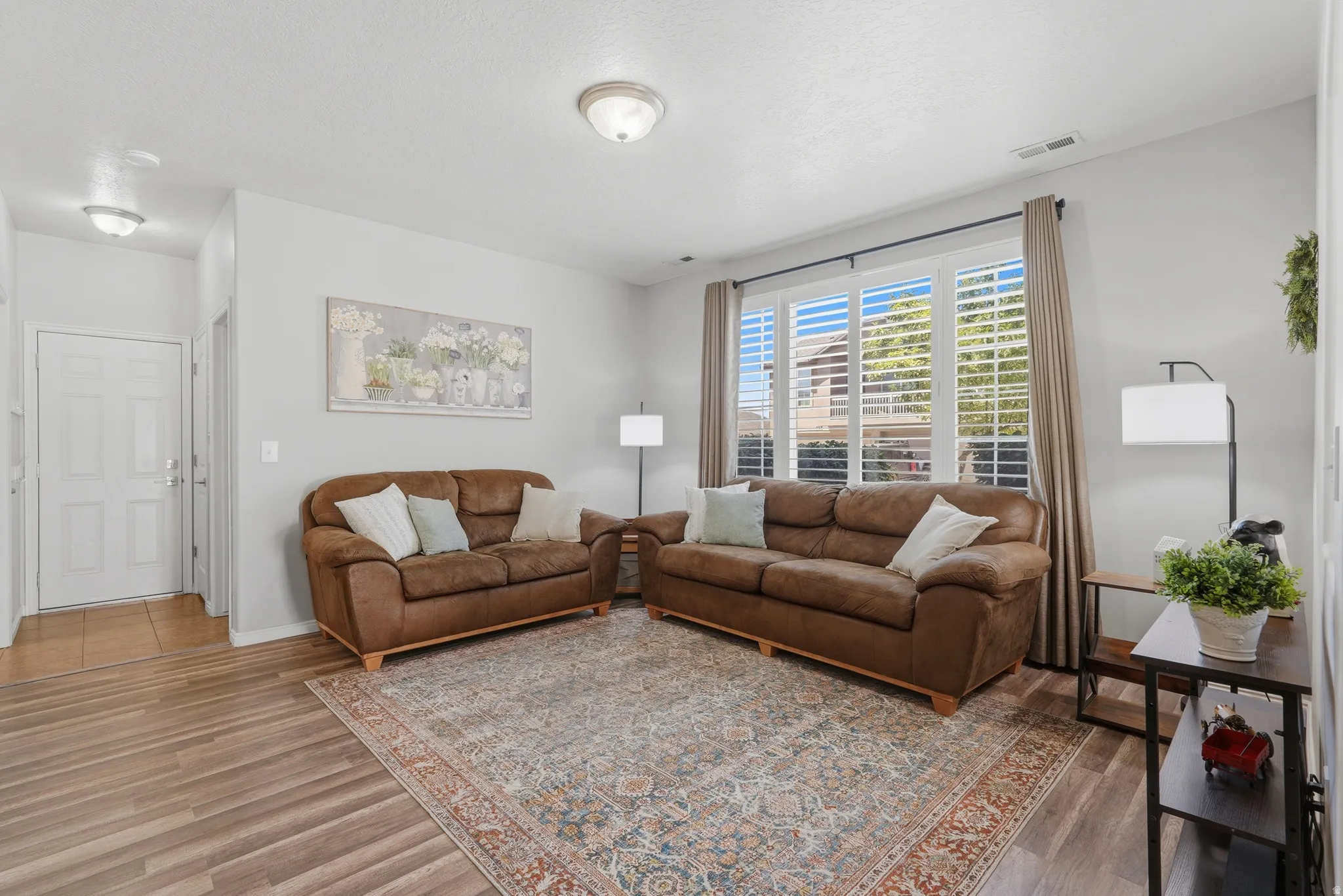 Living area featuring wood-finish flooring, light neutral wall paint, and a large window with white plantation shutters