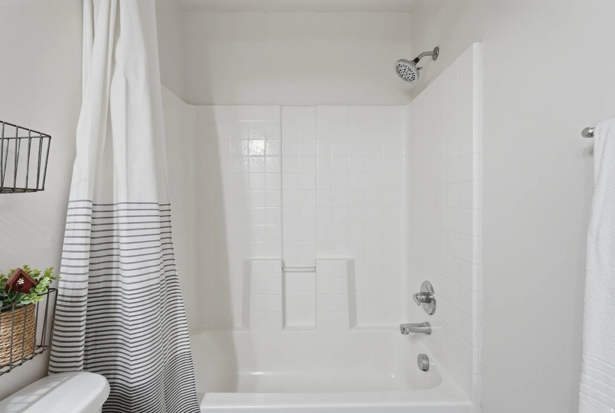 White tile shower and tub combination featuring chrome fixtures and a fixed showerhead