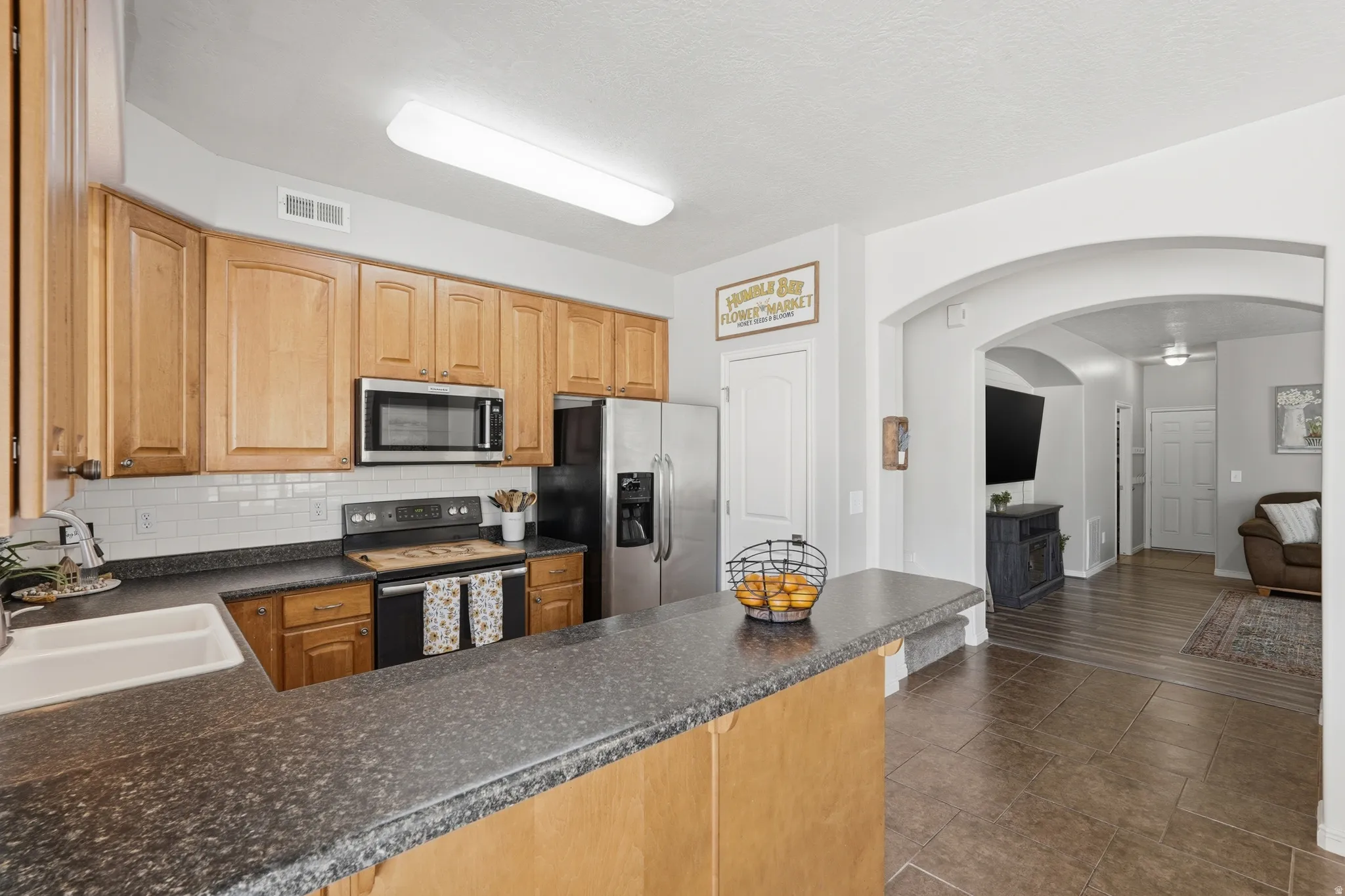 Kitchen featuring wood cabinetry, dark speckled countertops, stainless steel appliances, and a white subway tile backsplash