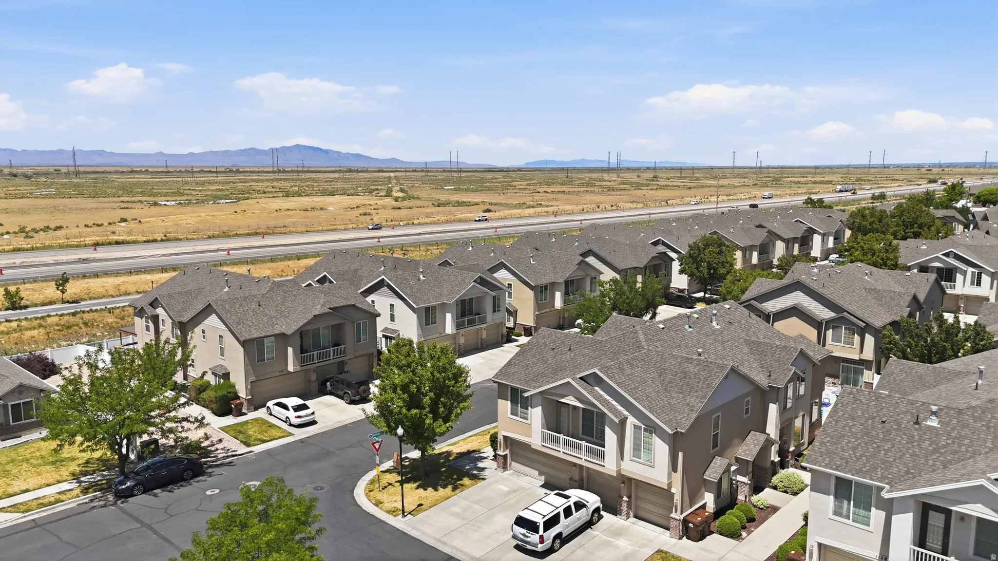 Residential streetscape featuring a curved asphalt road, mature trees, and a series of two-story homes with attached garages