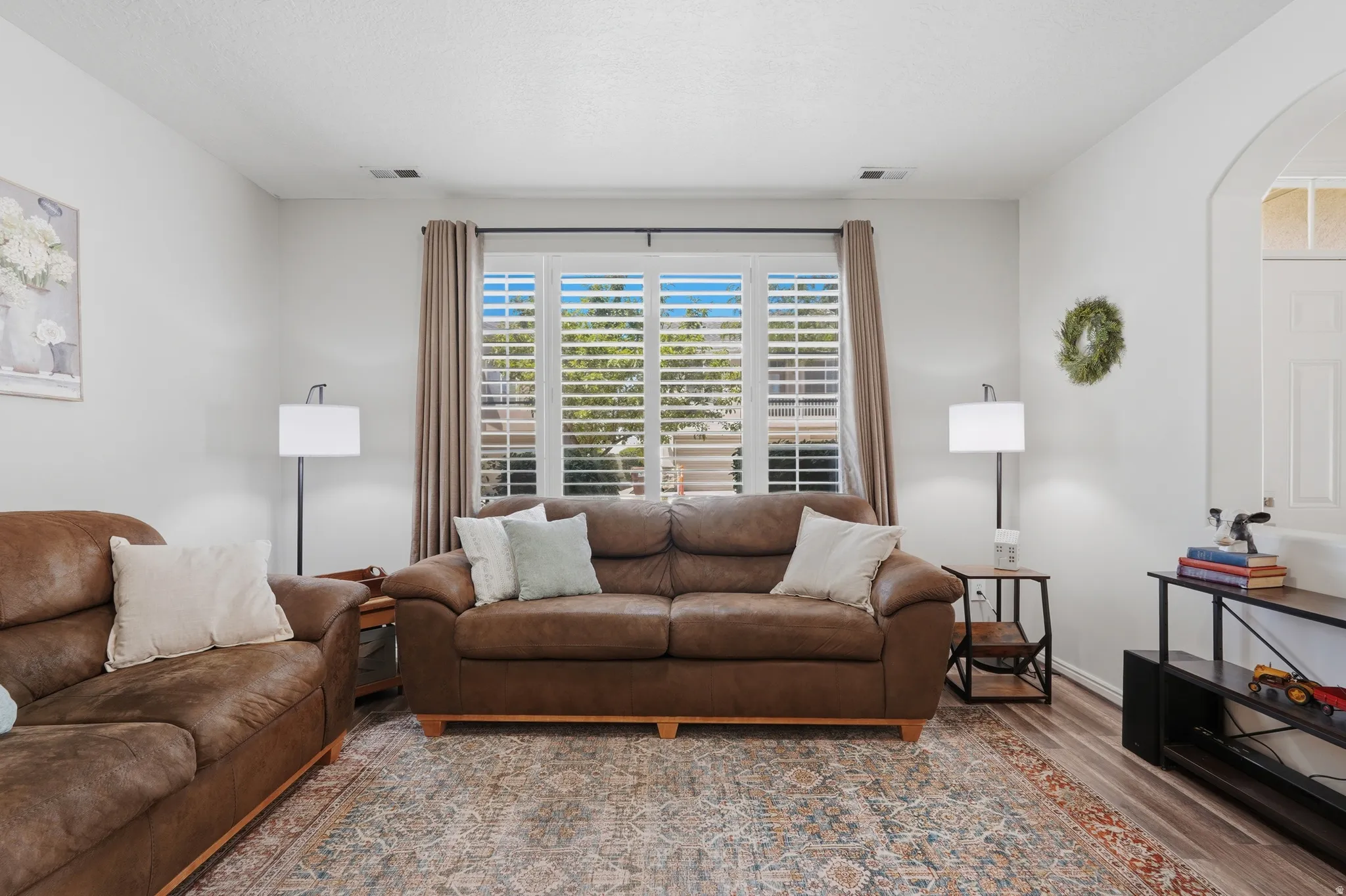 Living area featuring wood-finish flooring, white walls, and a large window with plantation shutters