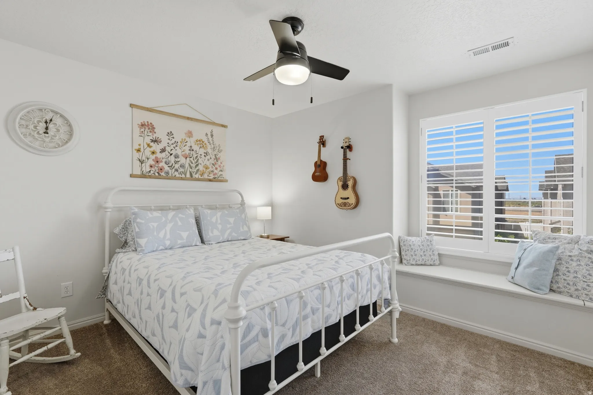 Bedroom featuring a window seat with white plantation shutters, a ceiling fan with integrated lighting, and carpet flooring