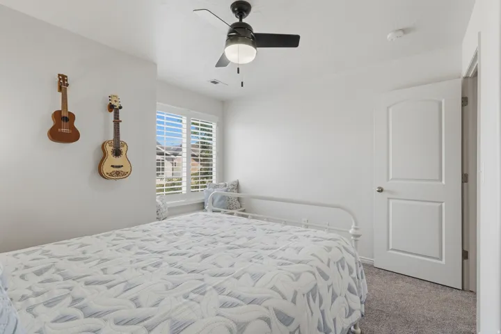 Bedroom featuring a window with plantation shutters, a black ceiling fan with integrated lighting, a white paneled interior door, and gray carpet flooring