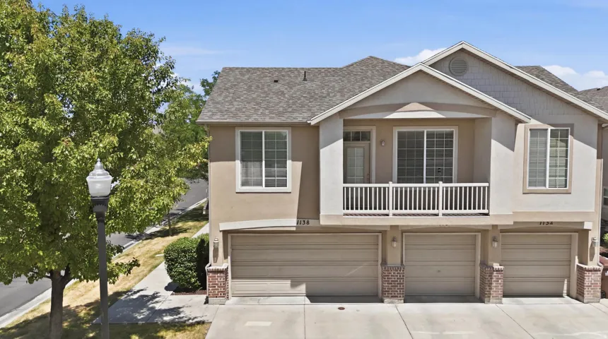 Multi-level townhouse exterior featuring stucco siding, a gabled roof, and attached garages with panel doors