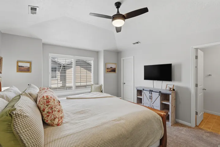 Vaulted ceiling bedroom featuring a ceiling fan with integrated lighting, window with white louvered shutters, and light-toned carpeting