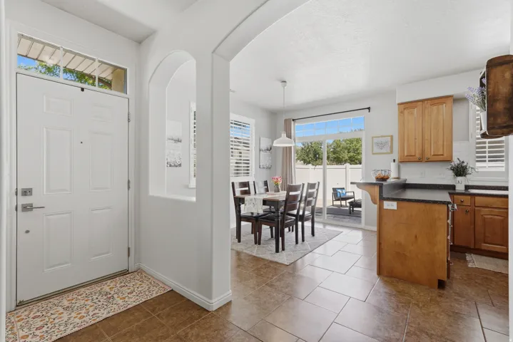 Entryway featuring a transom window, leading to a dining area with sliding glass doors to the patio, kitchen with wood cabinetry, and tile flooring throughout