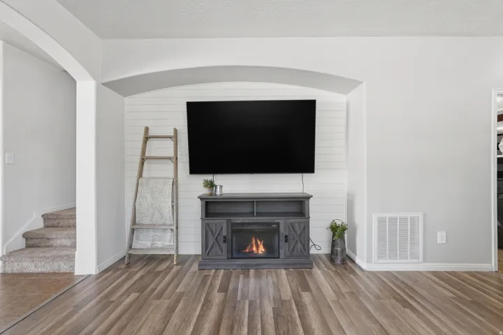 Living area featuring wood-finish flooring, a built-in electric fireplace with shiplap accent wall, and arched doorways