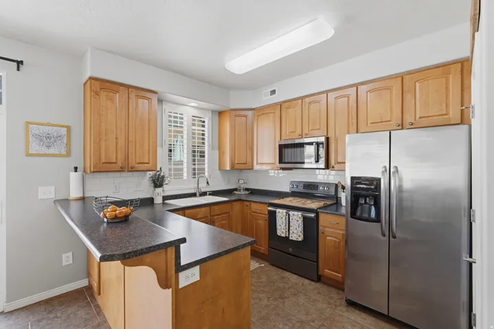 Kitchen featuring wood cabinetry, dark countertops, a white subway tile backsplash, stainless steel appliances, and a breakfast bar
