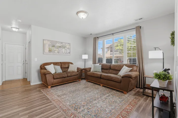 Living area featuring wood-finish flooring, light neutral wall paint, and a large window with white plantation shutters