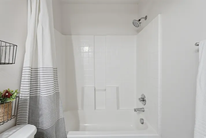White tile shower and tub combination featuring chrome fixtures and a fixed showerhead