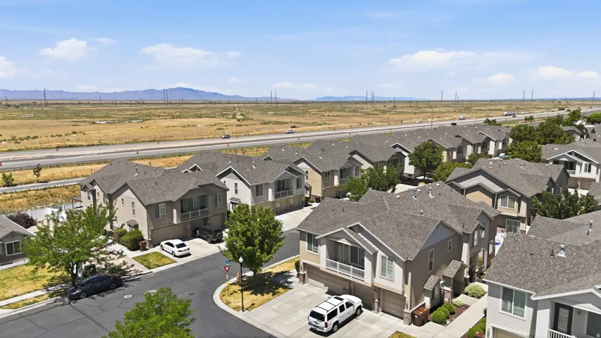 Residential streetscape featuring a curved asphalt road, mature trees, and a series of two-story homes with attached garages