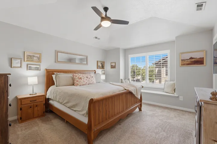 Carpeted bedroom featuring a tray ceiling, ceiling fan, and a window seat with plantation shutters