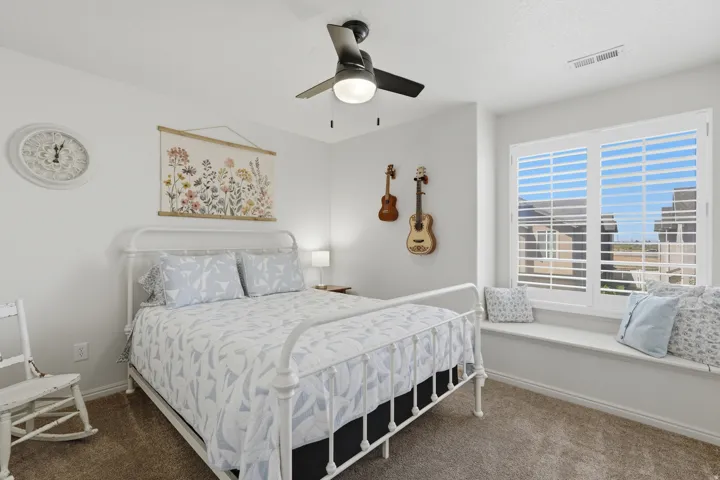 Bedroom featuring a window seat with white plantation shutters, a ceiling fan with integrated lighting, and carpet flooring