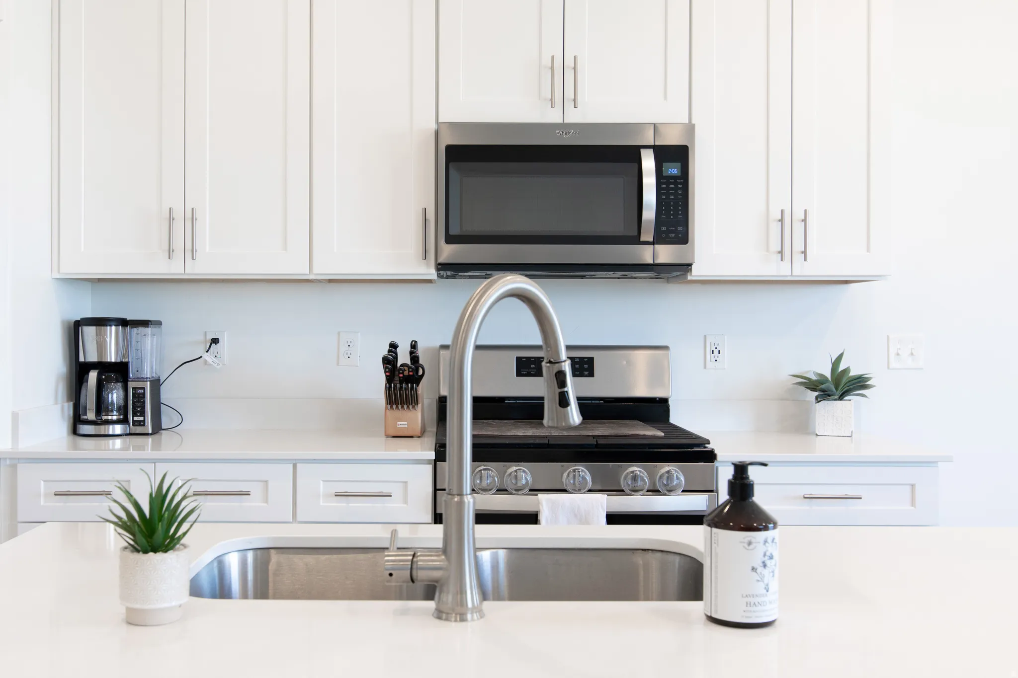 Bright kitchen featuring white cabinetry, stainless steel appliances, a stainless steel sink with a gooseneck faucet, and light-toned countertops