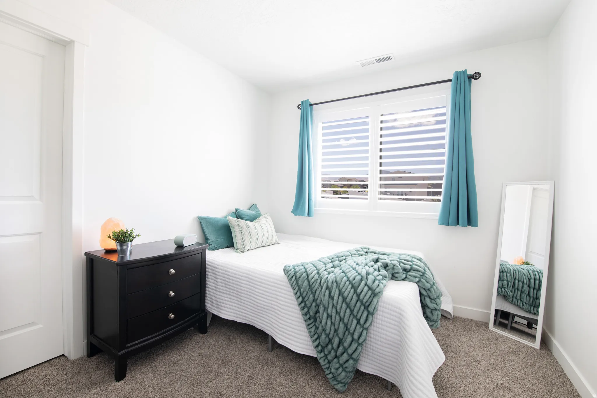 Bright interior space featuring a window with white louvered shutters, white baseboards, and neutral carpet flooring