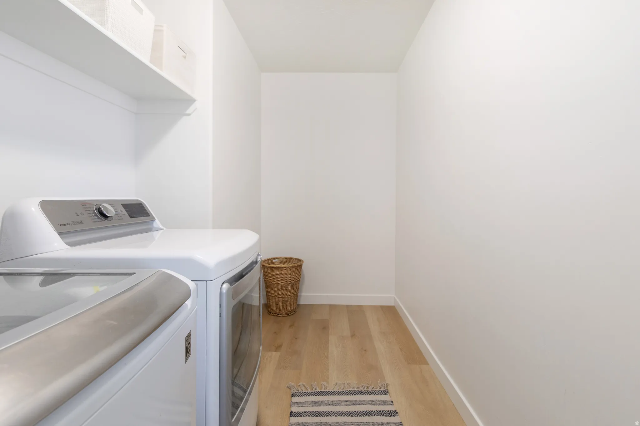 Dedicated laundry area featuring a white appliance set, a single white floating shelf, light wood-finish flooring, and white wall finishes