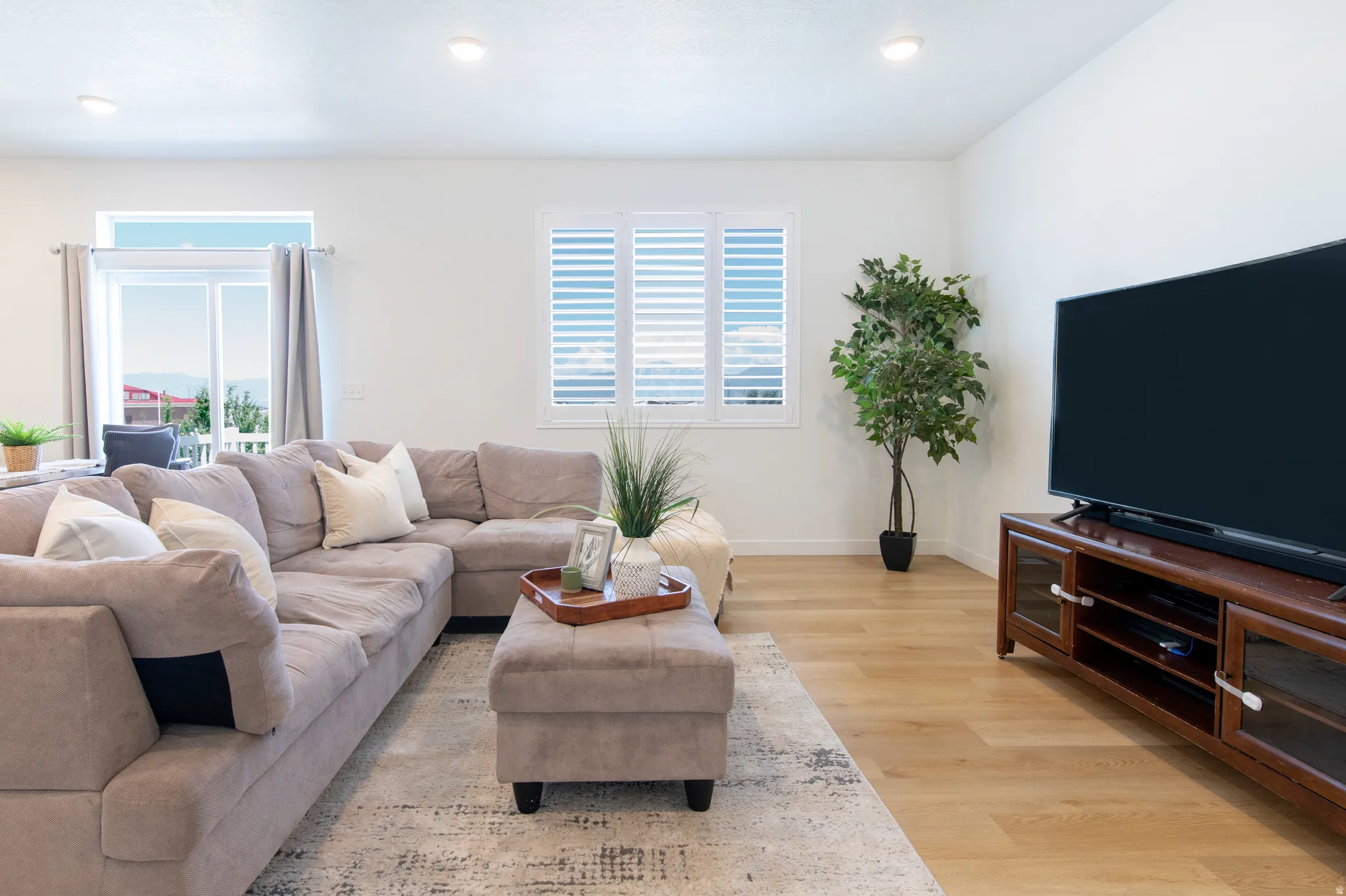 Bright living area featuring wood-finish flooring, recessed lighting, and a window with plantation shutters