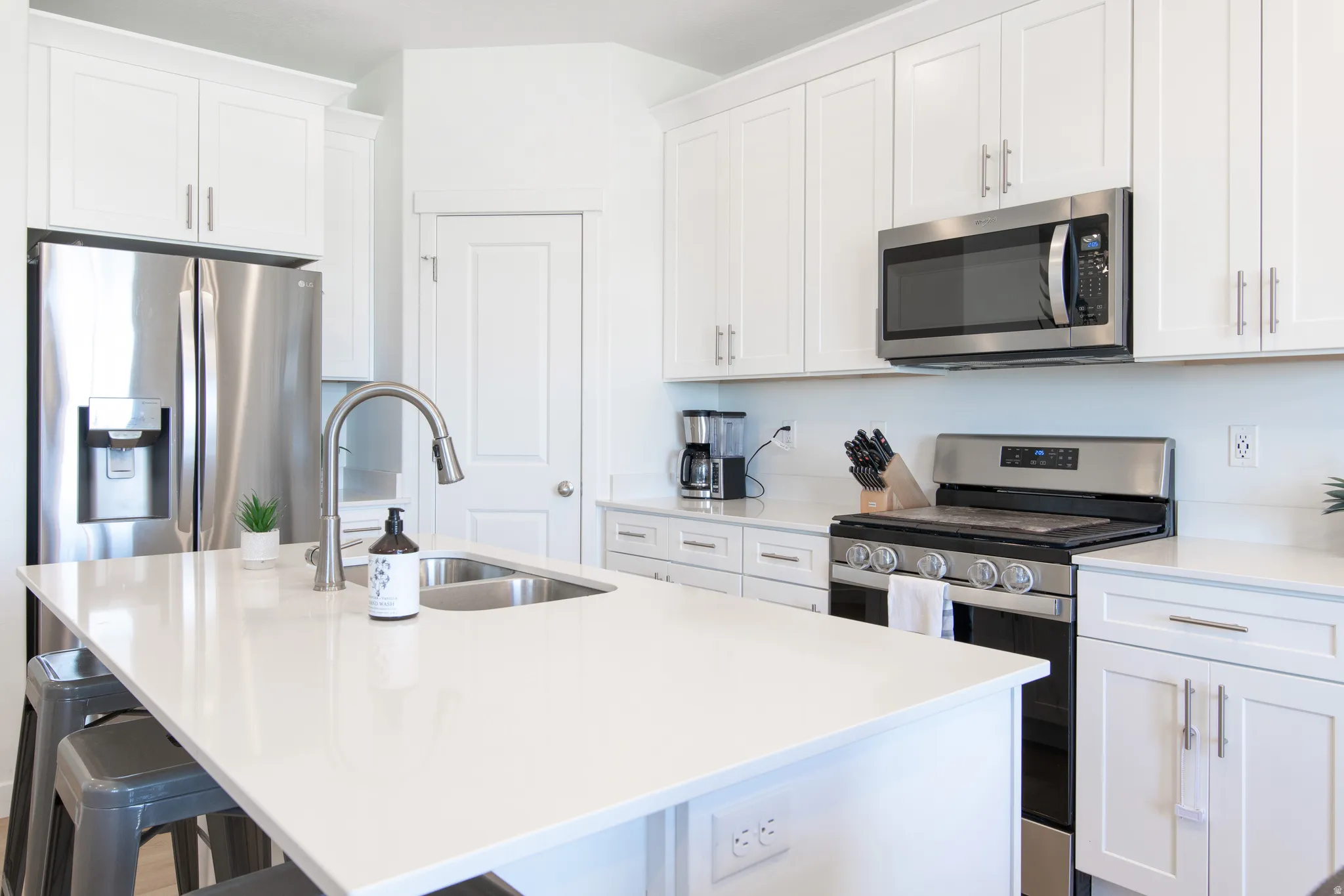 Kitchen featuring white cabinetry, stainless steel appliances, a center island with an undermount sink, and light-toned countertops