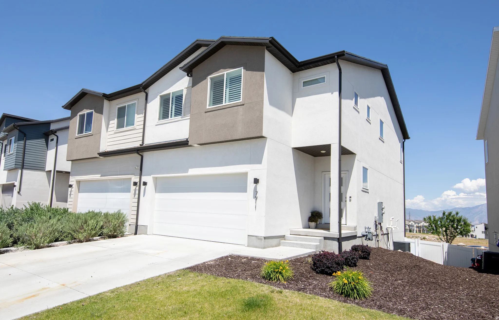 Contemporary multi-story residence featuring a two-car garage, white stucco siding, and dark trim accents