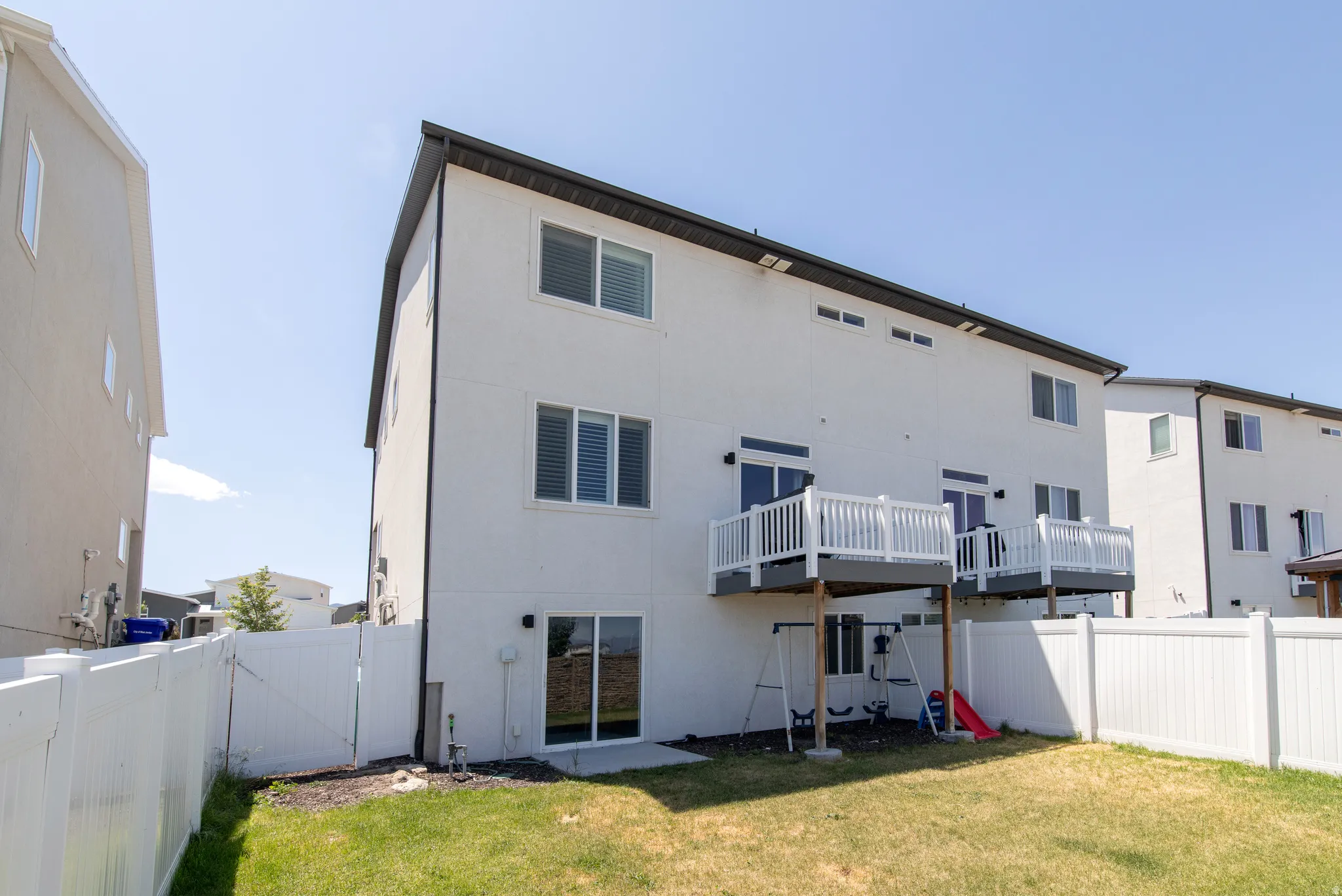 Fenced backyard featuring two upper-level balconies with white railings, a lower-level sliding glass door, and a ground-level patio