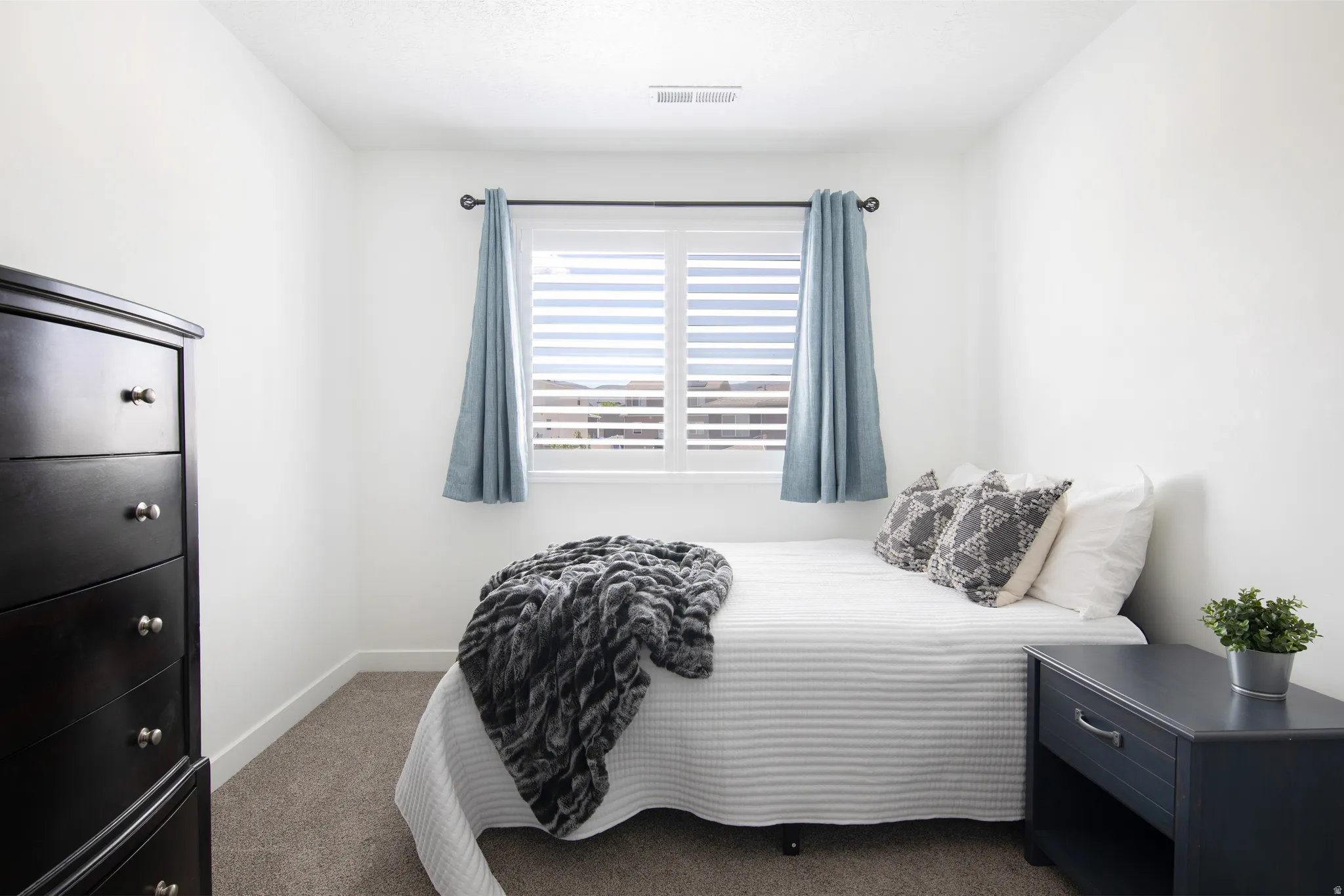 Bedroom featuring an exterior window with plantation shutters and drapes, neutral wall paint, and carpeting