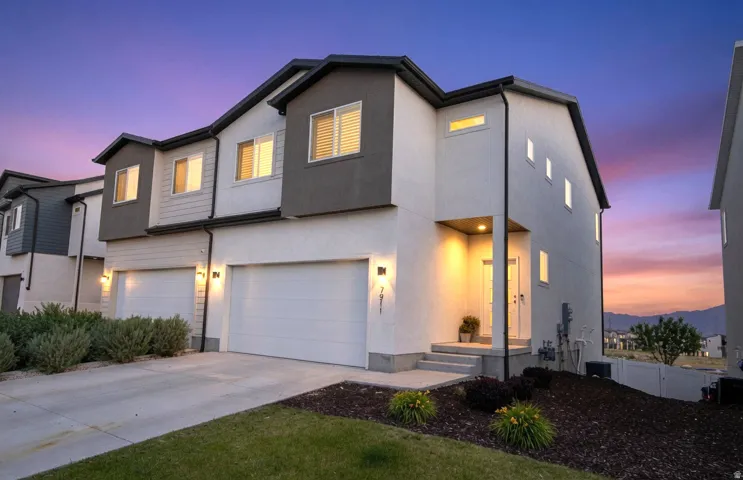 Contemporary townhome exterior featuring a two-car garage, white stucco and gray siding, and a covered entry with built-in lighting