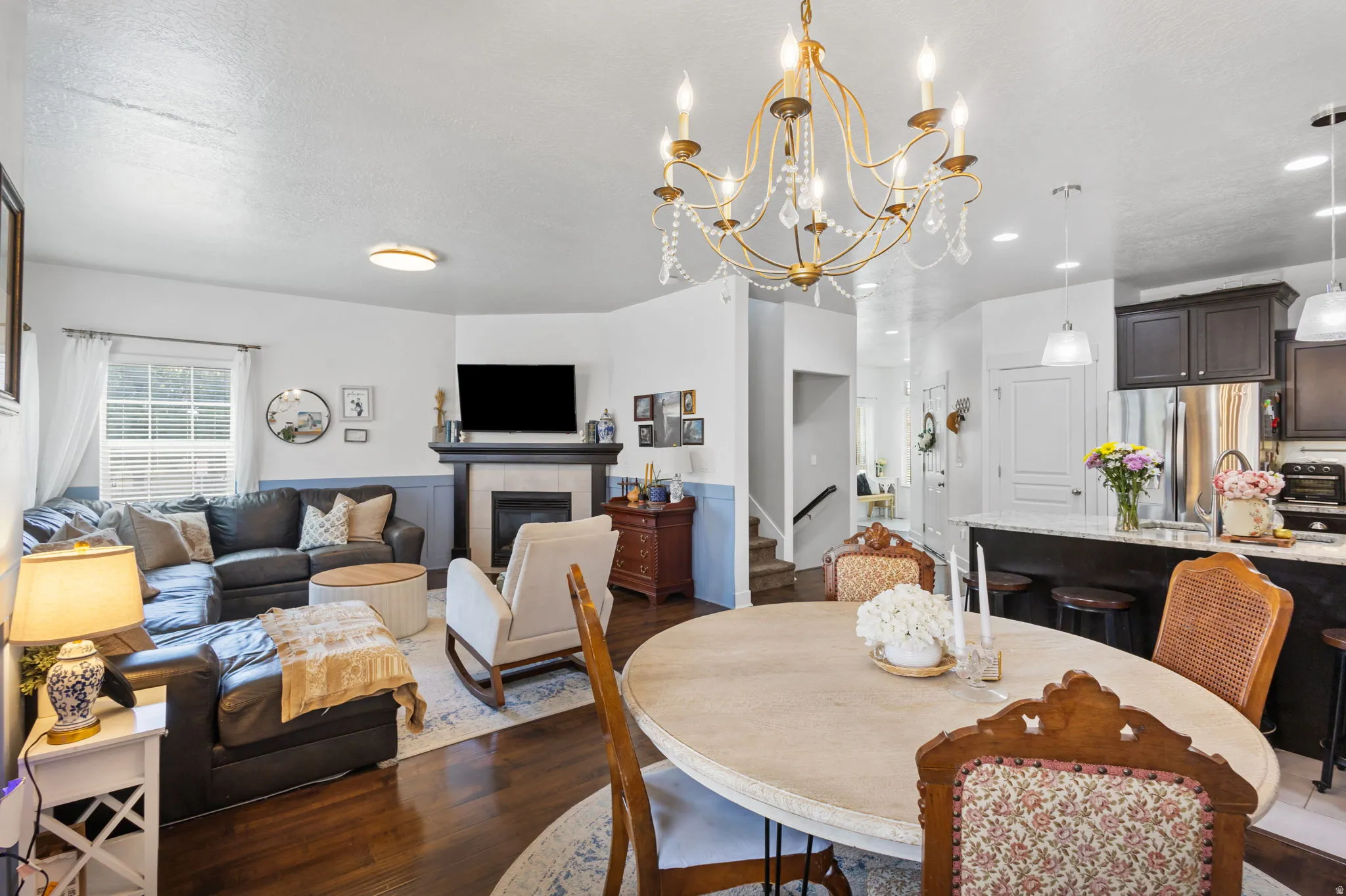 Open-concept living space featuring wood-finish flooring, a fireplace with a tiled surround and dark wood mantel, and a kitchen island with a light-toned countertop
