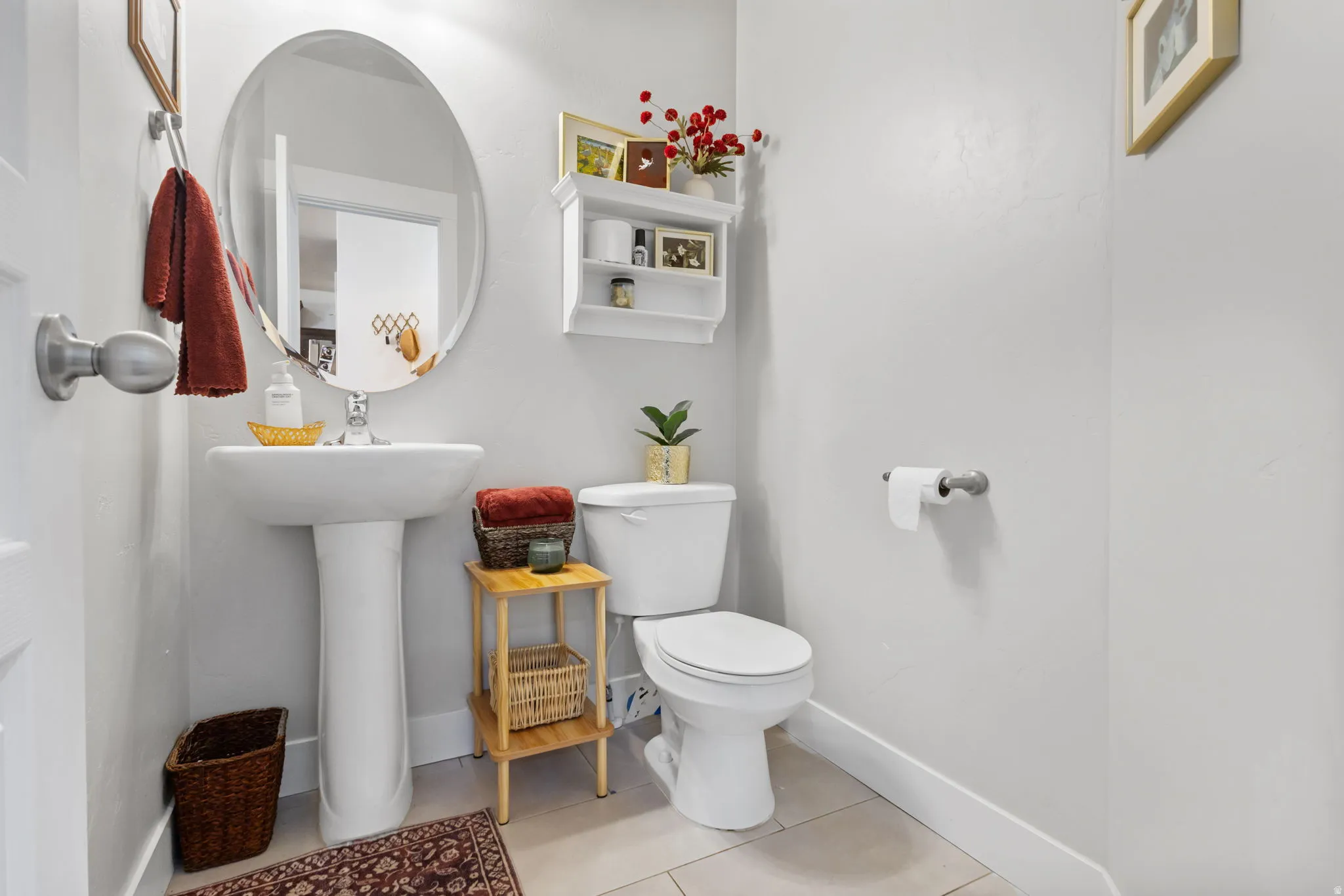 Powder room featuring a pedestal sink with chrome faucet, an oval wall-mounted mirror, and light-toned tile flooring