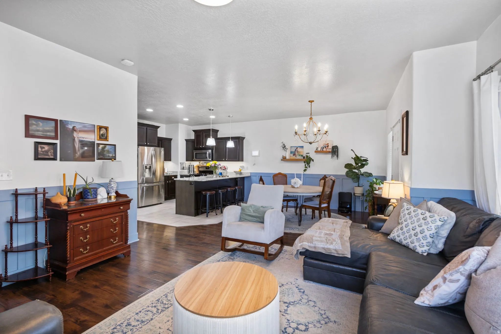Open-concept living space featuring wood-finish flooring, a kitchen with dark cabinetry and stainless steel appliances, and a dining area with a chandelier