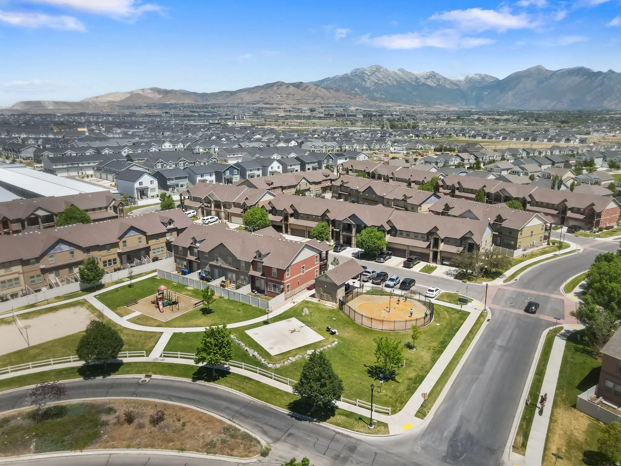 Expansive community featuring multi-story residential buildings with pitched roofs, a central green space with a playground, and paved streets