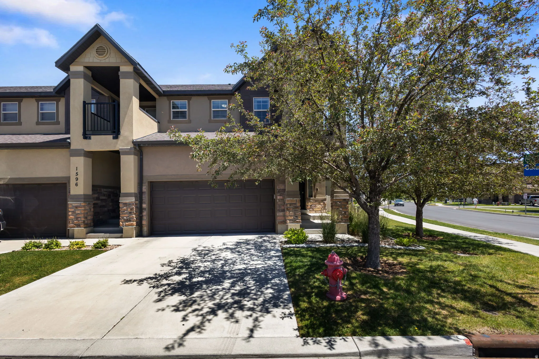 Two-story residence featuring a stucco and stone veneer exterior, an integrated single-car garage, a covered entry with an upper-level balcony, and a concrete driveway