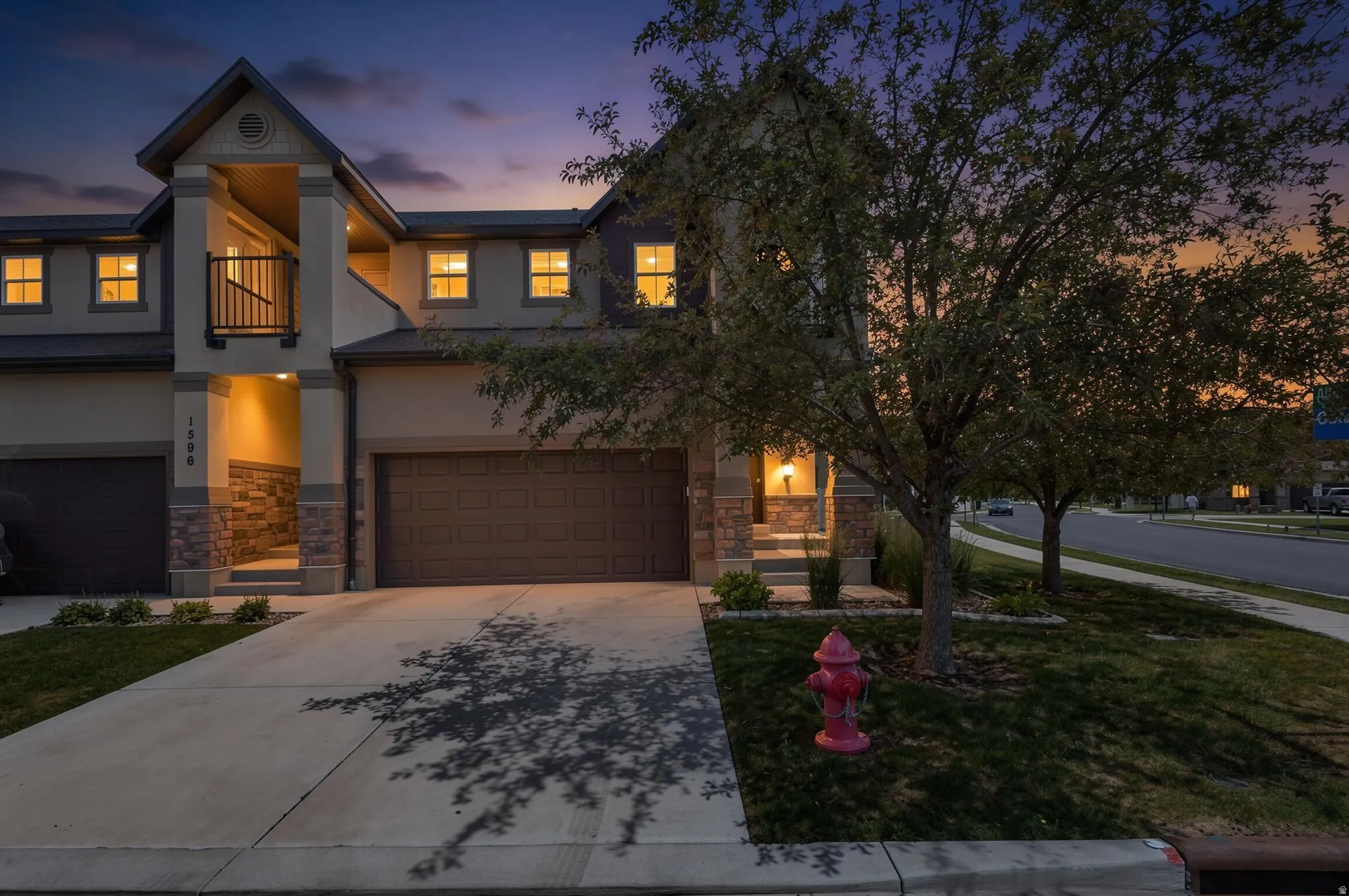 Multi-story residential facade featuring stone accents, a private balcony with a dark railing, and a two-car garage