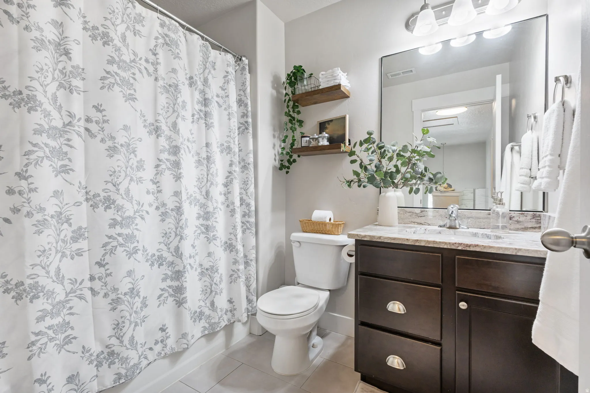 Bathroom featuring a dark wood vanity with a light-colored countertop, an integrated sink with a chrome faucet, a framed mirror, and a shower with a patterned curtain