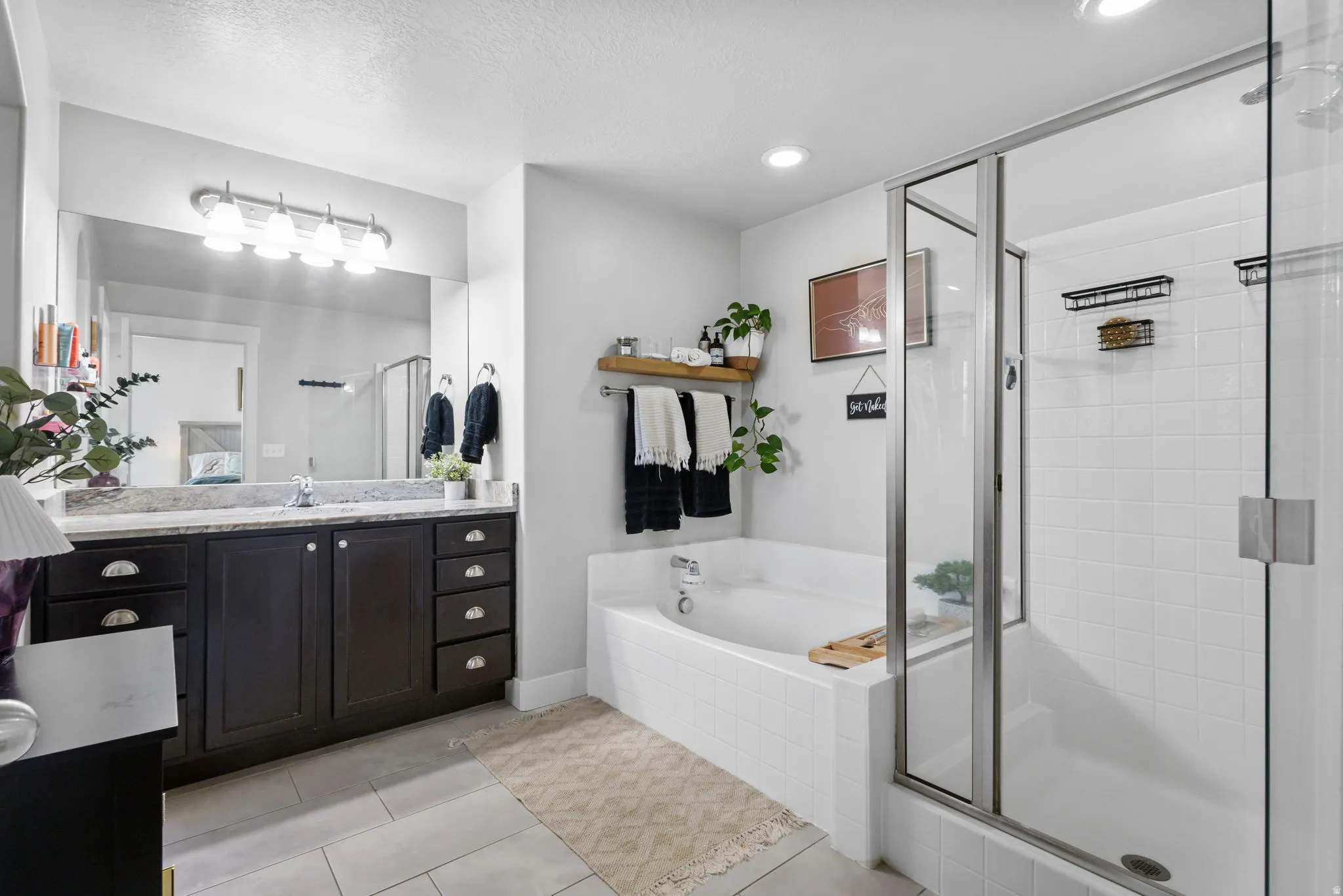 Bathroom featuring a spacious soaking tub, glass-enclosed shower with white subway tile, and a dual vanity with a light-toned countertop