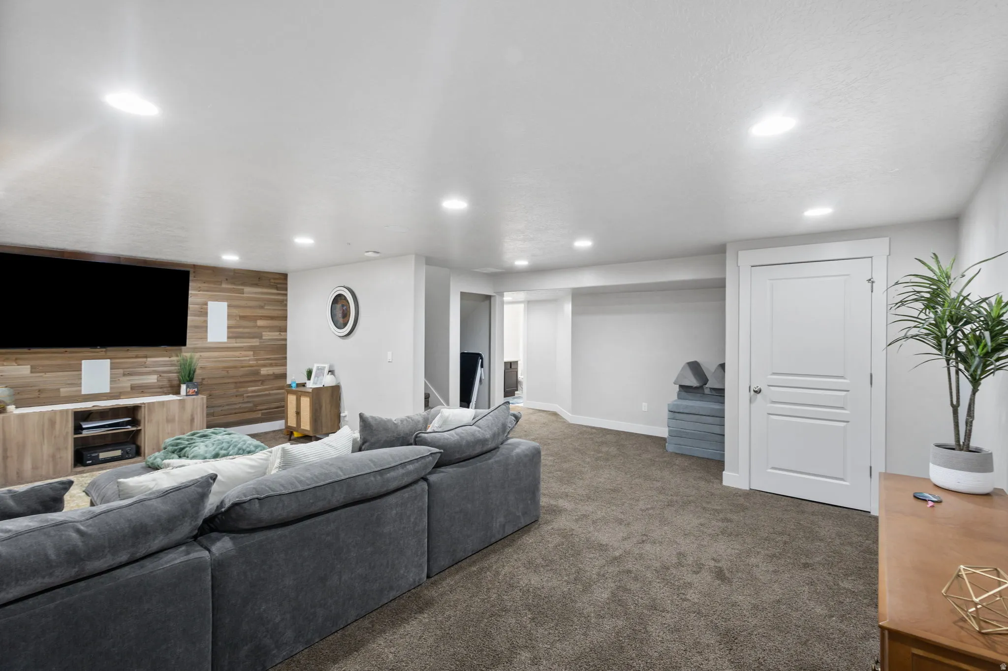Spacious entertainment area featuring a wood-panel accent wall, recessed lighting, and neutral carpeting